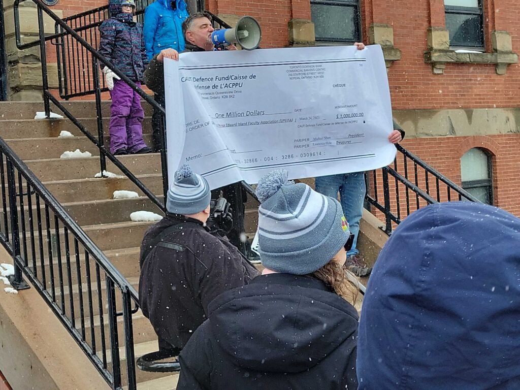 A man (Larry Hale) holding a large novelty cheque on the steps of a building.