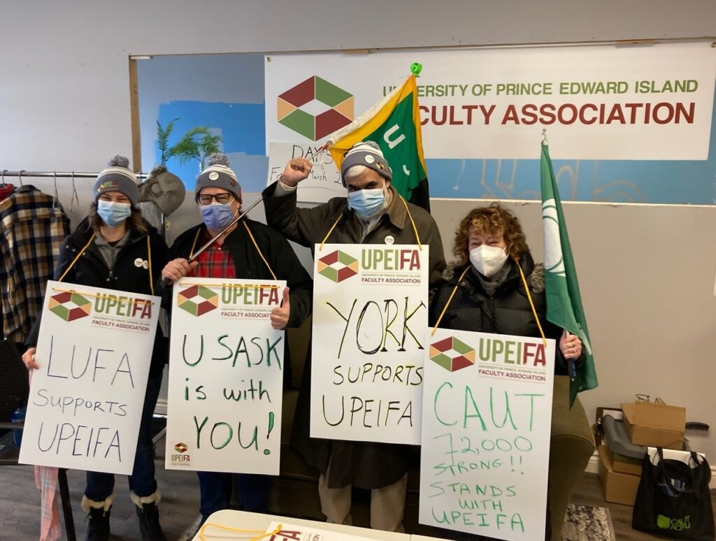 A group of four picketers holding picket signs and flags. 