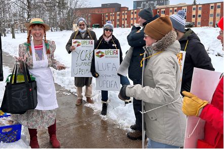 A group of picketers with picket signs talking to a woman dressed as Anne of Green Gables.