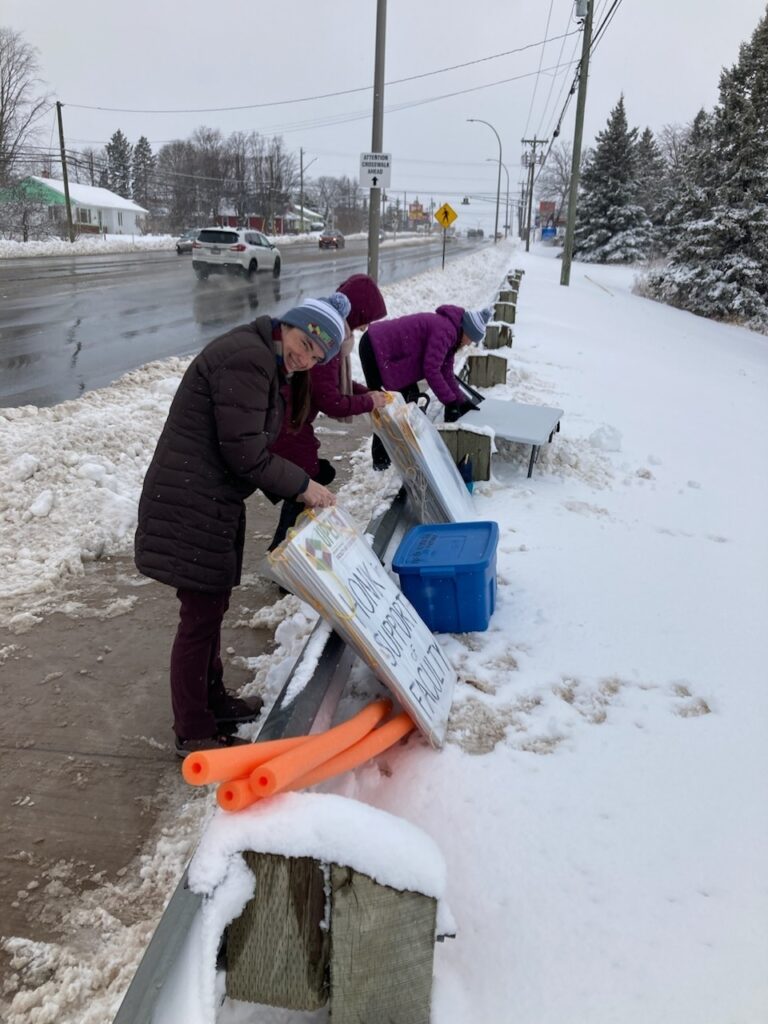 Picketers setting up signs and a table at a picket line in the snow.